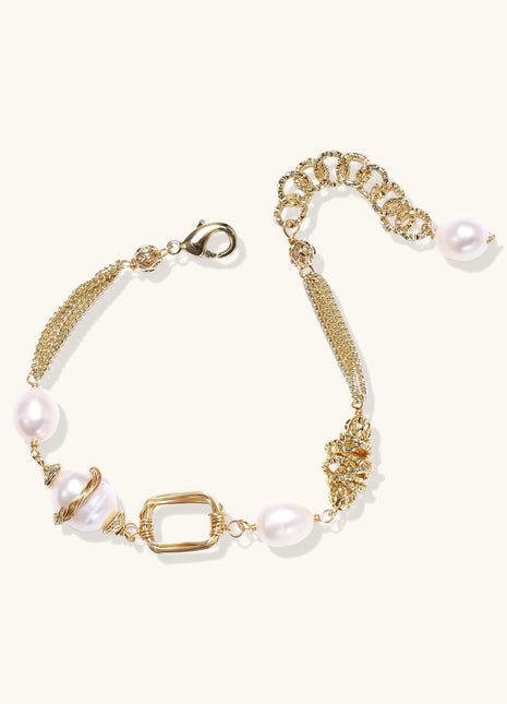 Gold-plated bracelet featuring cream freshwater pearls and decorative chain links on white background.