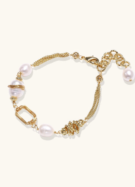Gold-plated bracelet featuring cream freshwater pearls and decorative chain links on white background.