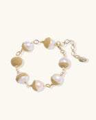 Adjustable bracelet featuring baroque pearls wrapped in gold mesh wire with delicate chain links on cream background.