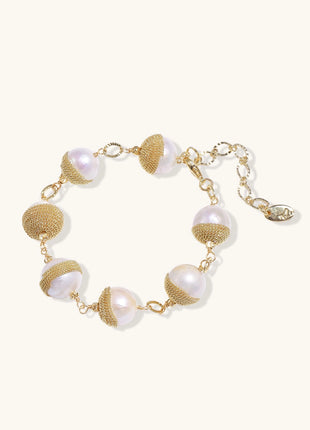 Adjustable bracelet featuring baroque pearls wrapped in gold mesh wire with delicate chain links on cream background.