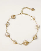 Delicate gold chain bracelet featuring iridescent shell charms with freshwater pearls on white background.