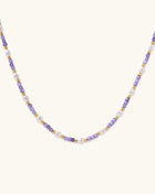 Delicate beaded necklace with alternating purple zirconia stones, white freshwater pearls, and gold-plated spacers on cream background.