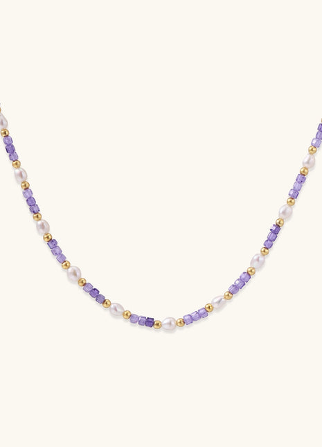 Delicate beaded necklace with alternating purple zirconia stones, white freshwater pearls, and gold-plated spacers on cream background.