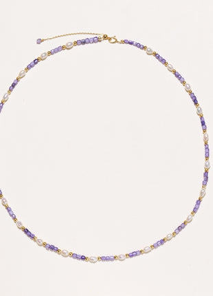 Delicate beaded necklace with alternating purple zirconia stones, white freshwater pearls, and gold-plated spacers on cream background.
