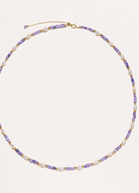 Delicate beaded necklace with alternating purple zirconia stones, white freshwater pearls, and gold-plated spacers on cream background.
