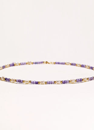 Delicate beaded necklace with alternating purple zirconia stones, white freshwater pearls, and gold-plated spacers on cream background.
