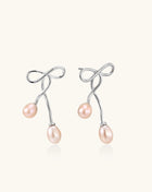 Delicate sterling silver wire earrings with organic bow shapes and two pink freshwater pearls on white background