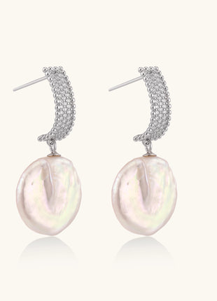 Sterling silver huggie earrings with lustrous baroque pearls displaying iridescent pink and cream tones on white background.