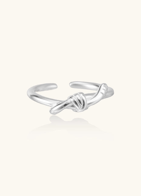 Delicate sterling silver ring with geometric knot design on white background, showcasing adjustable open band.