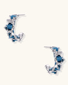 Crescent-shaped gold-plated hoop earrings with blue crystals set in organic vine-like metalwork on white background.