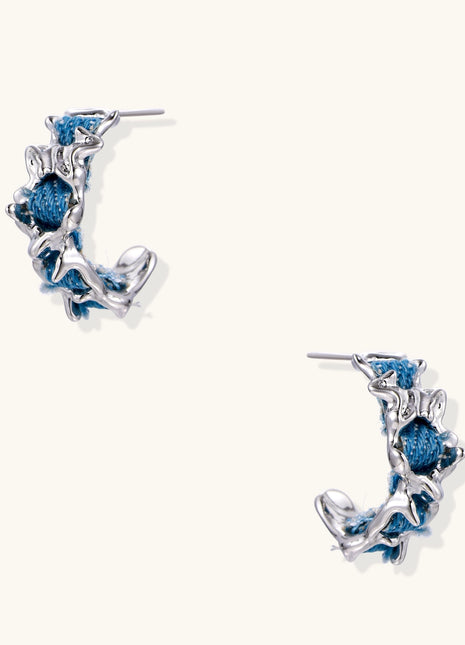 Crescent-shaped gold-plated hoop earrings with blue crystals set in organic vine-like metalwork on white background.