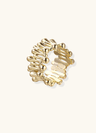 Close-up of chunky 18K gold-plated brass ring with flowing wave-like sculptural design on neutral background.