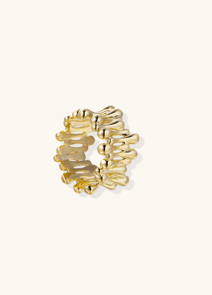Close-up of chunky 18K gold-plated brass ring with flowing wave-like sculptural design on neutral background.