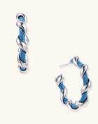 Twisted hoop earrings featuring blue denim fabric braided with gold-plated metal in a spiral design on white background.