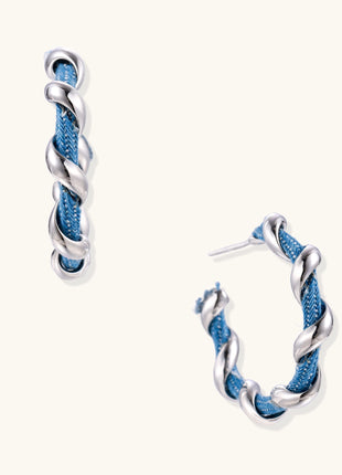 Twisted hoop earrings featuring blue denim fabric braided with gold-plated metal in a spiral design on white background.