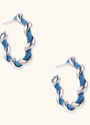 Twisted hoop earrings featuring blue denim fabric braided with gold-plated metal in a spiral design on white background.