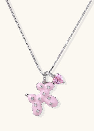 Pink enamel cross pendant with zirconia crystals and teardrop charm on 18K gold-plated chain against white background