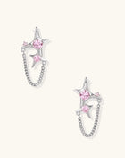 Gold-plated star earrings with pink zirconia stones connected by delicate chains on light background