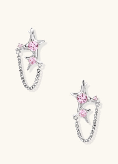 Gold-plated star earrings with pink zirconia stones connected by delicate chains on light background