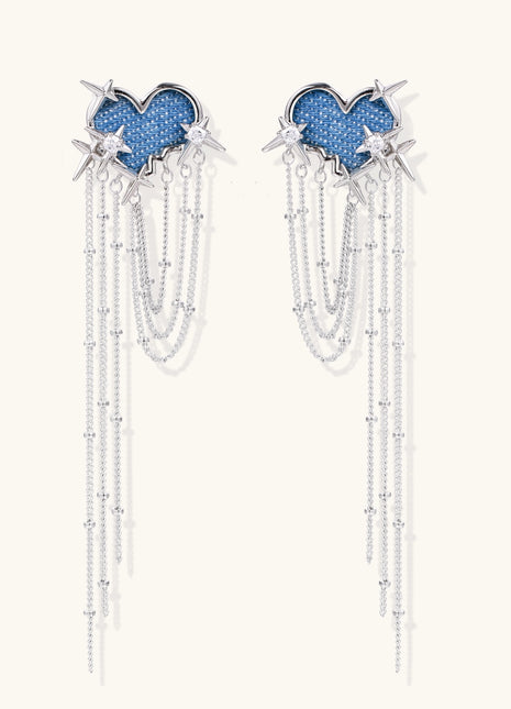 Long dangle earrings with blue denim heart shapes, silver star spikes, and multiple cascading chains on beige background.