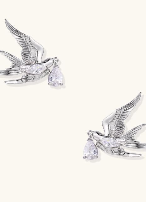 Gold-plated brass swallow earrings with detailed wing engravings carrying clear zirconia crystal drops in their beaks