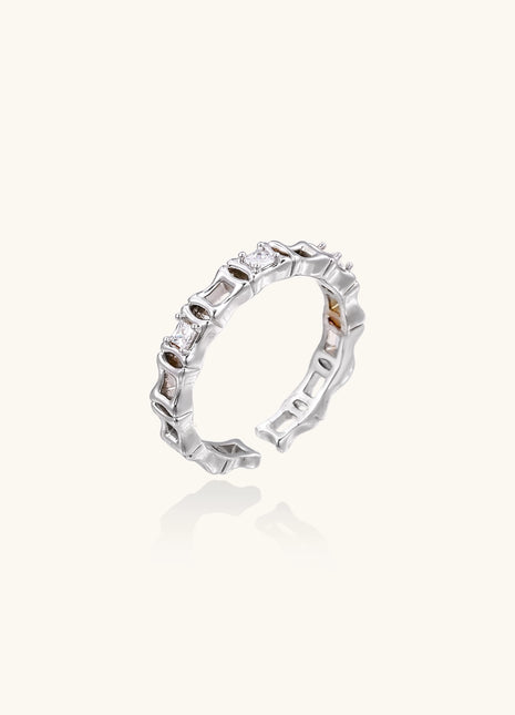 Close-up of geometric gold-plated ring with alternating rectangular blocks and zirconia crystals on white background.