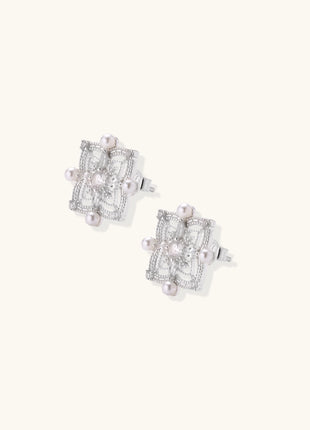 Detailed view of sterling silver stud earrings with geometric filigree design and small freshwater pearls on white background.