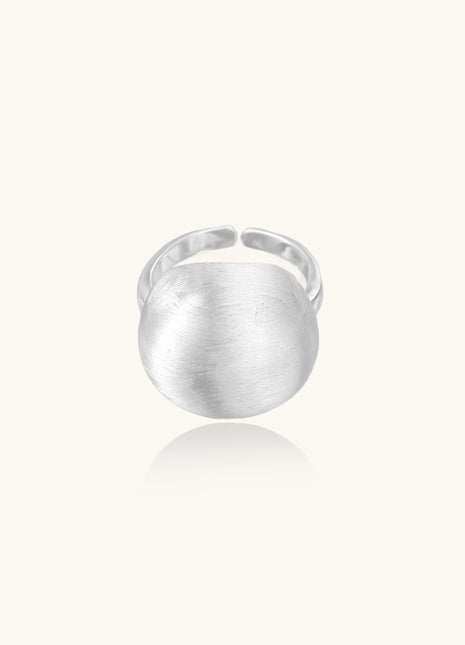 Minimalist sterling silver ring with large brushed disc top and adjustable band on white background.