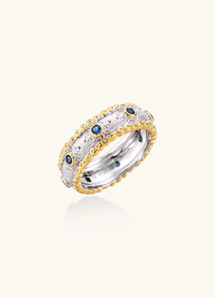 Sterling silver ring with brushed center band, blue zirconia stones, and 24k gold-plated decorative borders.