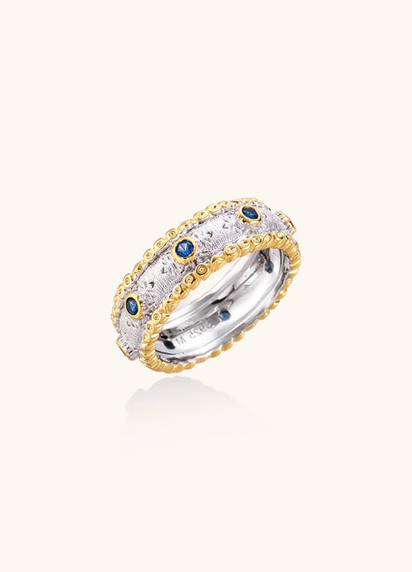 Sterling silver ring with brushed center band, blue zirconia stones, and 24k gold-plated decorative borders.