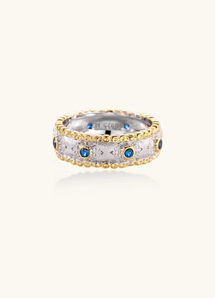 Sterling silver ring with brushed center band, blue zirconia stones, and 24k gold-plated decorative borders.