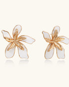 Large floral stud earrings with gold-plated brass petals and white enamel centers on neutral background