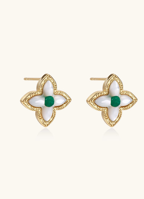 Dainty gold-plated quatrefoil stud earrings with white mother-of-pearl petals and green gemstone centers on beige background.