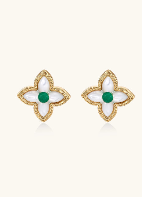 Dainty gold-plated quatrefoil stud earrings with white mother-of-pearl petals and green gemstone centers on beige background.