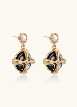 Gold-plated drop earrings with cross design framing iridescent abalone shell and pearl studs on neutral background.