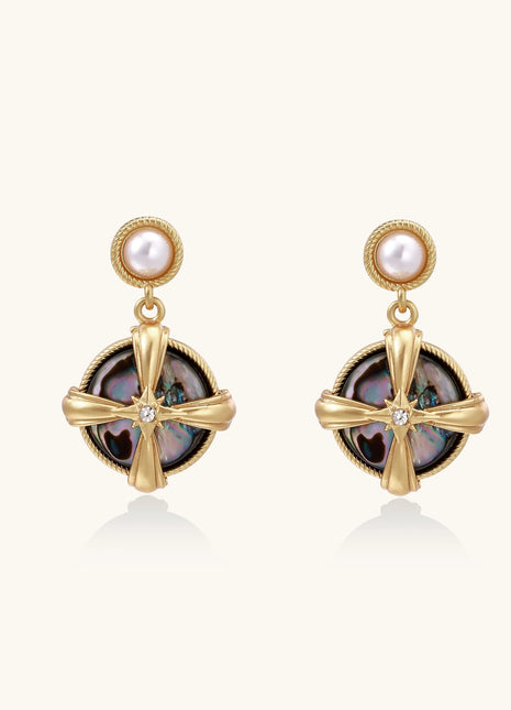 Gold-plated drop earrings with cross design framing iridescent abalone shell and pearl studs on neutral background.
