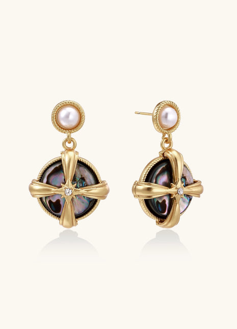 Gold-plated drop earrings with cross design framing iridescent abalone shell and pearl studs on neutral background.