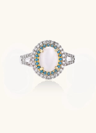 Gold-plated ring with oval cat's eye stone center, blue accent stones, and crystal halo on white background.