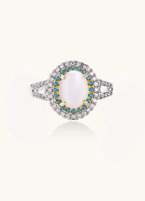 Gold-plated ring with oval cat's eye stone center, blue accent stones, and crystal halo on white background.