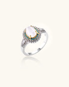 Gold-plated ring with oval cat's eye stone center, blue accent stones, and crystal halo on white background.