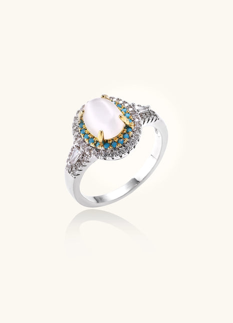 Gold-plated ring with oval cat's eye stone center, blue accent stones, and crystal halo on white background.