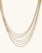 Multiple delicate gold-plated snake chains in graduated lengths on white background, adjustable layered necklace design.