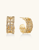 Close-up of geometric gold-plated hoop earrings with crystal pave in intricate lattice pattern on neutral background.