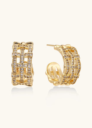 Close-up of geometric gold-plated hoop earrings with crystal pave in intricate lattice pattern on neutral background.