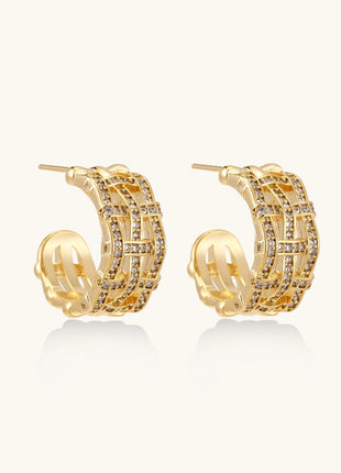 Close-up of geometric gold-plated hoop earrings with crystal pave in intricate lattice pattern on neutral background.