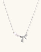 Dainty 14K gold plated necklace with freshwater pearls and sparkling bow charm on white background.