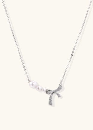 Dainty 14K gold plated necklace with freshwater pearls and sparkling bow charm on white background.