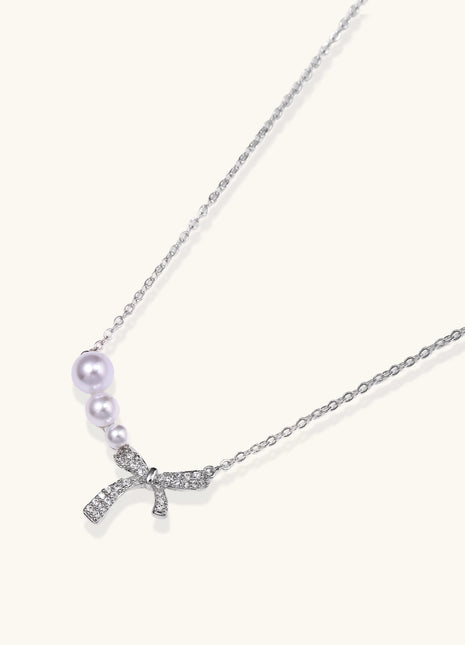 Dainty 14K gold plated necklace with freshwater pearls and sparkling bow charm on white background.