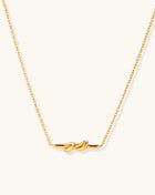 Dainty 18K gold plated stainless steel chain necklace with minimalist knot pendant on cream background.