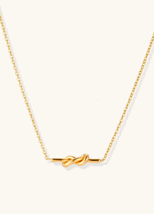 Dainty 18K gold plated stainless steel chain necklace with minimalist knot pendant on cream background.